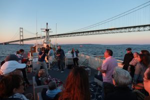 A photographer films a man speaking on board a Mackinac Island Sip ‘n Sail cruise as it passes near the Mackinac Bridge