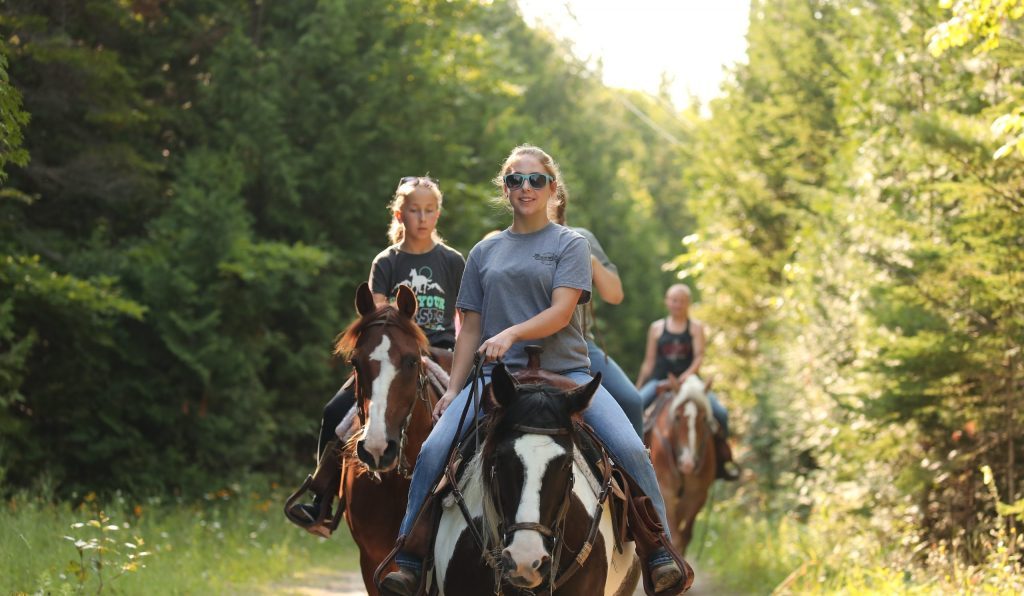 A group of girls ride horseback on a trail through the woods of Mackinac Island State Park