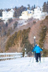 A couple goes cross-country skiing on a snowy day on Mackinac Island with cottages on the bluff in the background