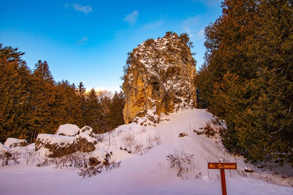 A “No Climbing” sign is posted at the foot of a snow-covered Sugar Loaf rock formation in Mackinac Island State Park