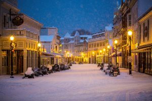 Snow blankets Main Street on Mackinac Island at night with streetlights aglow and snowmobiles lining the road