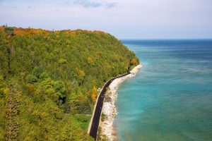 A view from above of Mackinac Island’s M-185 as it cuts between a forest of fall color and calm, blue water