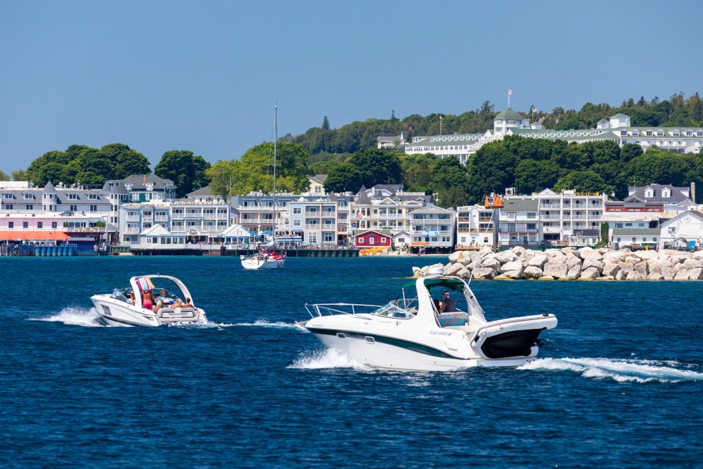 Personal boats motor through the Mackinac Island harbor with downtown in the background and Grand Hotel up on the bluff