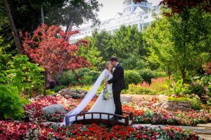 A bride and groom kiss while standing on a bridge in a gorgeous flower garden outside Mackinac Island's Grand Hotel