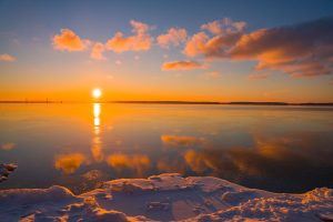 The sun sets beyond the Mackinac Bridge as seen from the snowy shore of Mackinac Island in winter