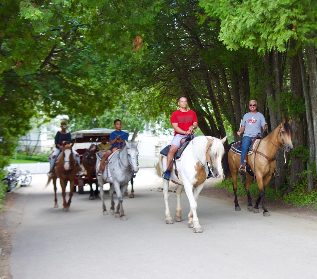 Mackinac Island visitors ride horseback on a paved road through Mackinac Island State Park