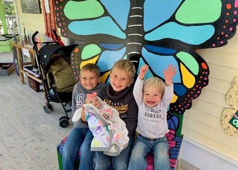 Four kids sit excitedly outside the Wings of Mackinac butterfly sign.