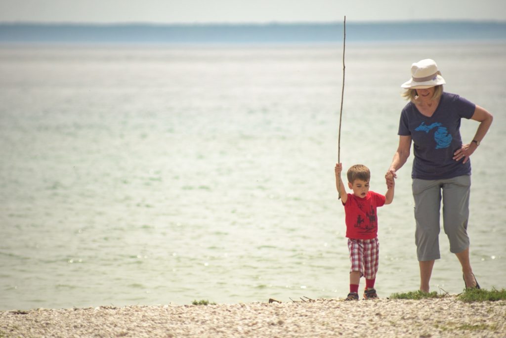 A grandmother holds a grandchild's hand as he raises a stick in the air on a rocky Mackinac Island beach