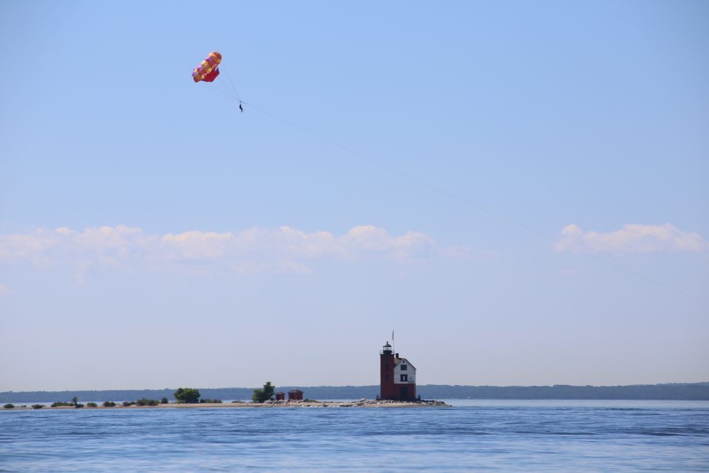 A parasailor soars over the blue water through clear skies above Round Island Lighthouse off Michigan’s Mackinac Island