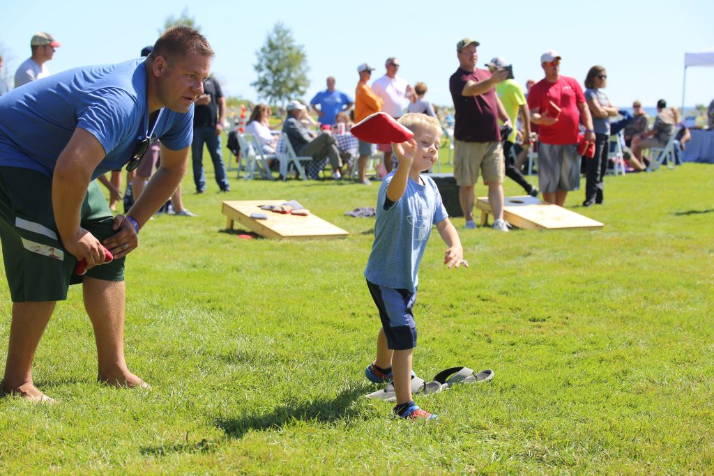 A young boy tosses a bean bag as a father looks on during a cornhole tournament on Mackinac Island