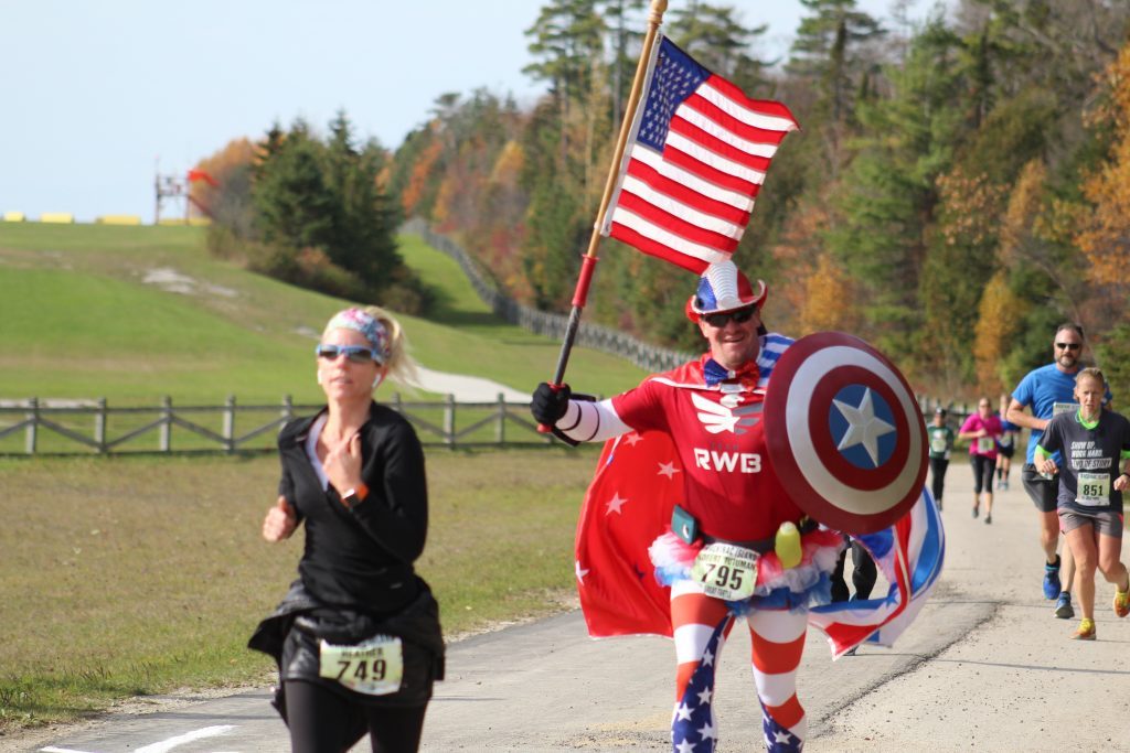 A man wearing a Captain America costume with a shield and American flag runs in Mackinac Island’s Great Turtle Trail Run