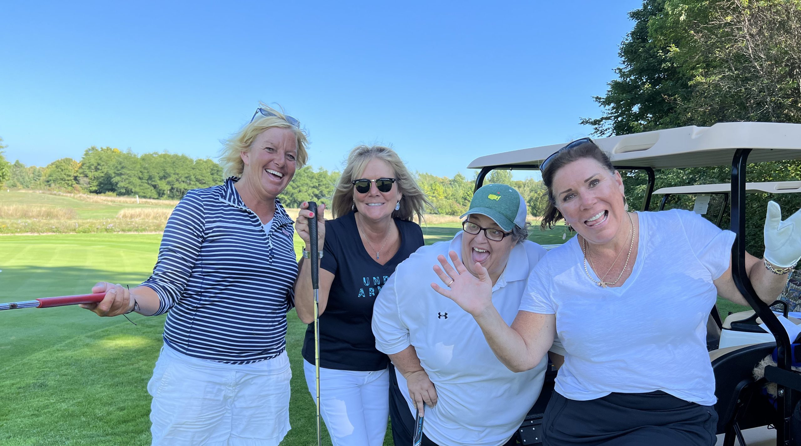 A foursome of ladies smiles by their golf cart at Mackinac Island's Wawashkamo Golf Club