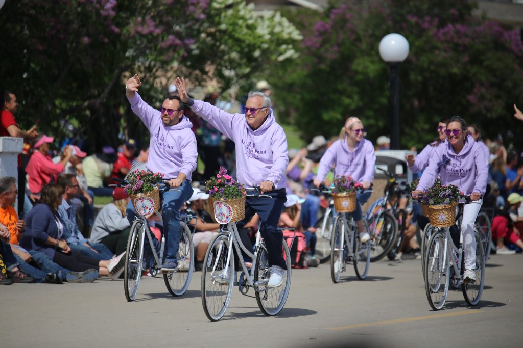 Bicyclists wearing lilac-colored sweatshirts pedal down the street in the annual Mackinac Island Lilac Parade