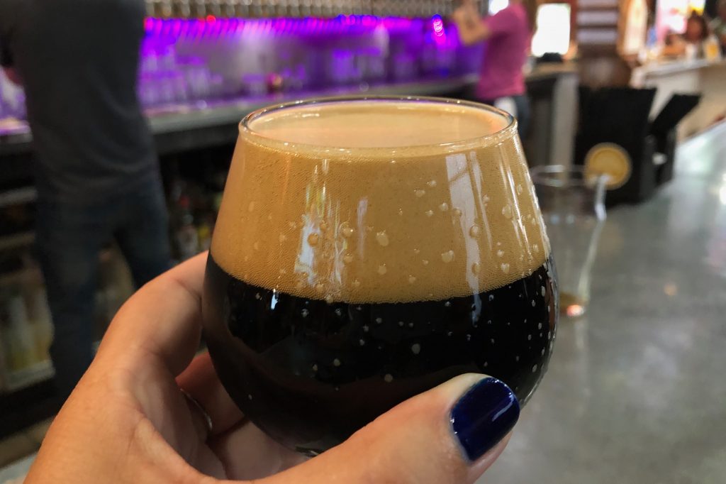 A hand holding a tulip glass of dark, foamy beer in a Mackinac Island bar