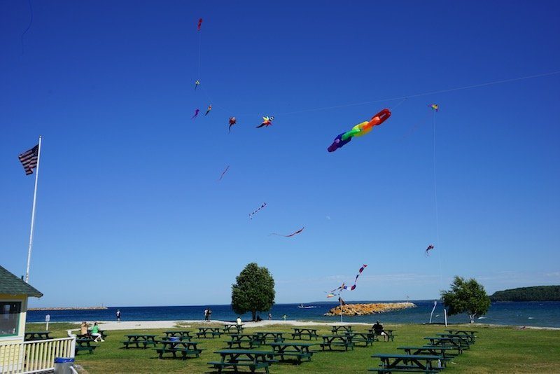 Colorful kites fly in the breeze above picnic tables on the green lawn of Mackinac Island’s Windermere Point