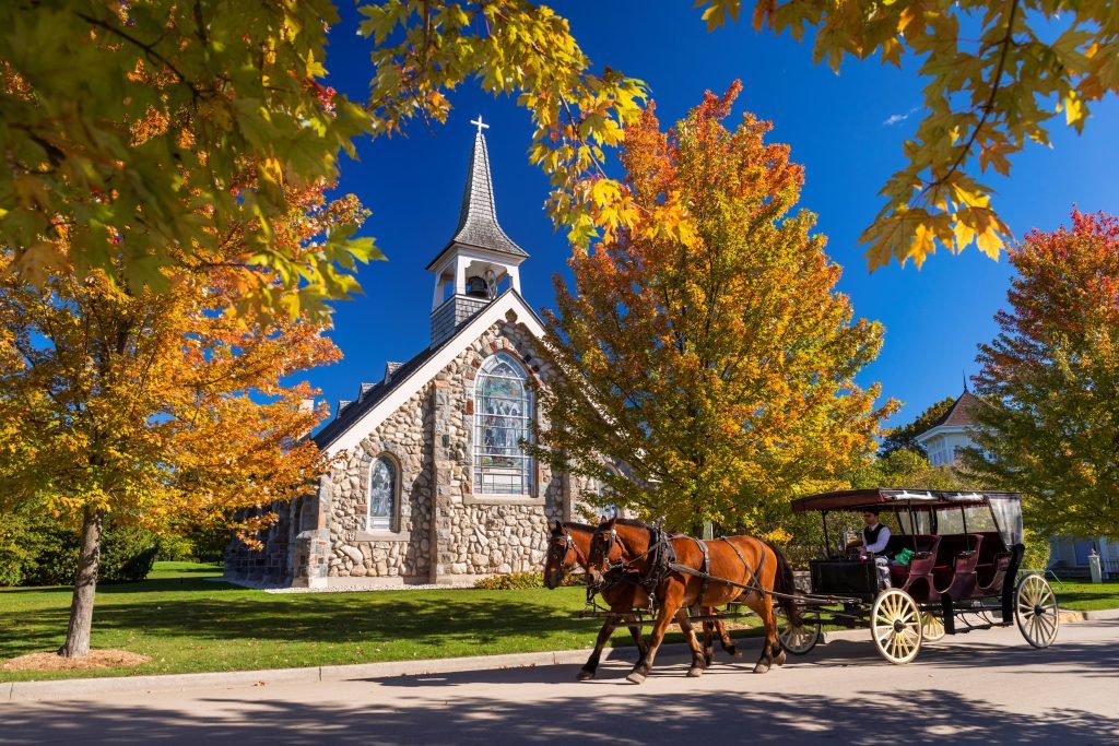 A horse-drawn carriage on Mackinac Island passes Little Stone Church amid gorgeous fall color