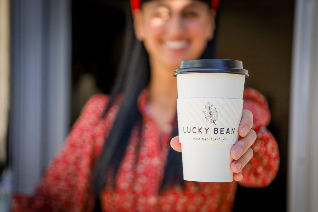 A barista wearing red holds out of a cup of coffee from Mackinac Island's Lucky Bean Coffee House