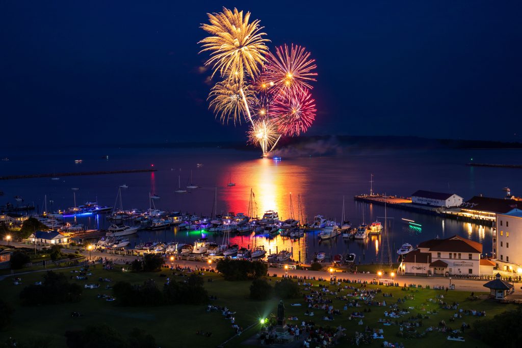 Fireworks launched from the Mackinac Island harbor light up the sky at night as a crowd watches from Marquette Park
