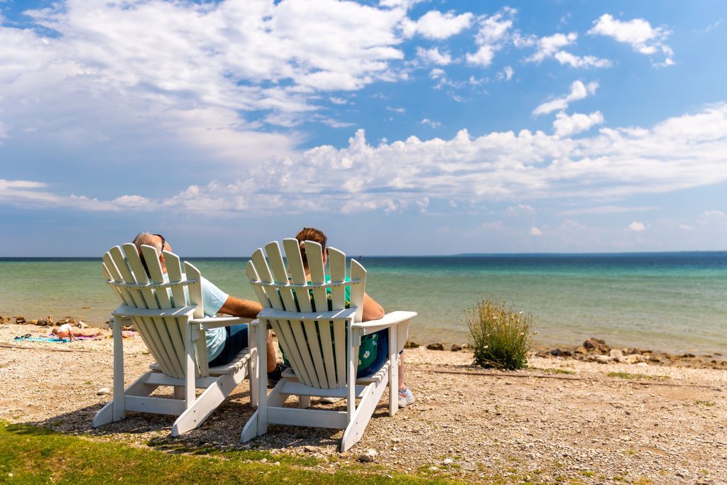 A couple relaxes on Adirondack chairs near the water on the beach at Mackinac Island’s Mission Point Resort