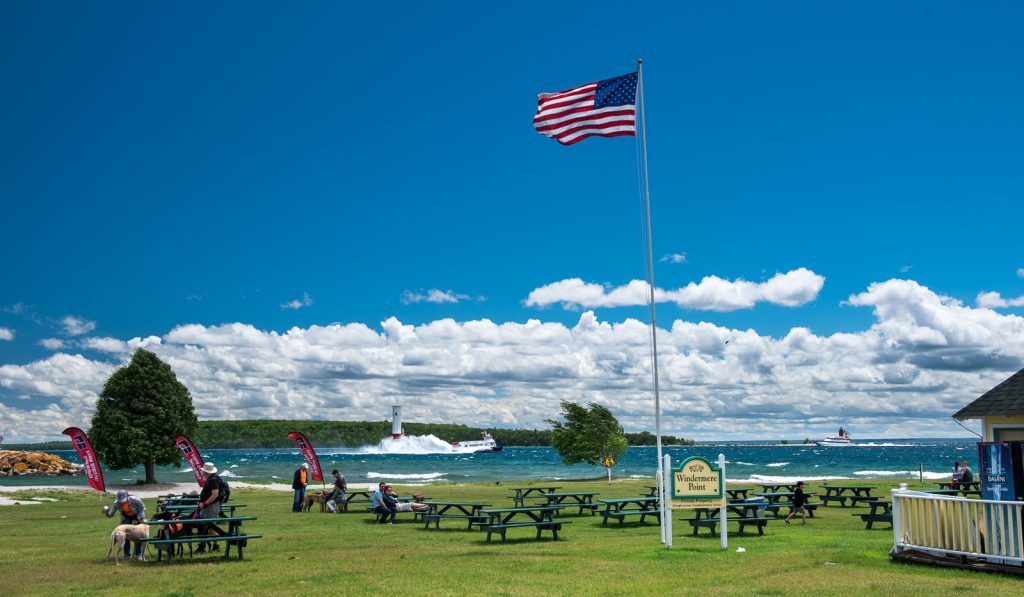 An American flag blows in the wind on Mackinac Island’s Windermere Point as people relax on picnic tables near the water