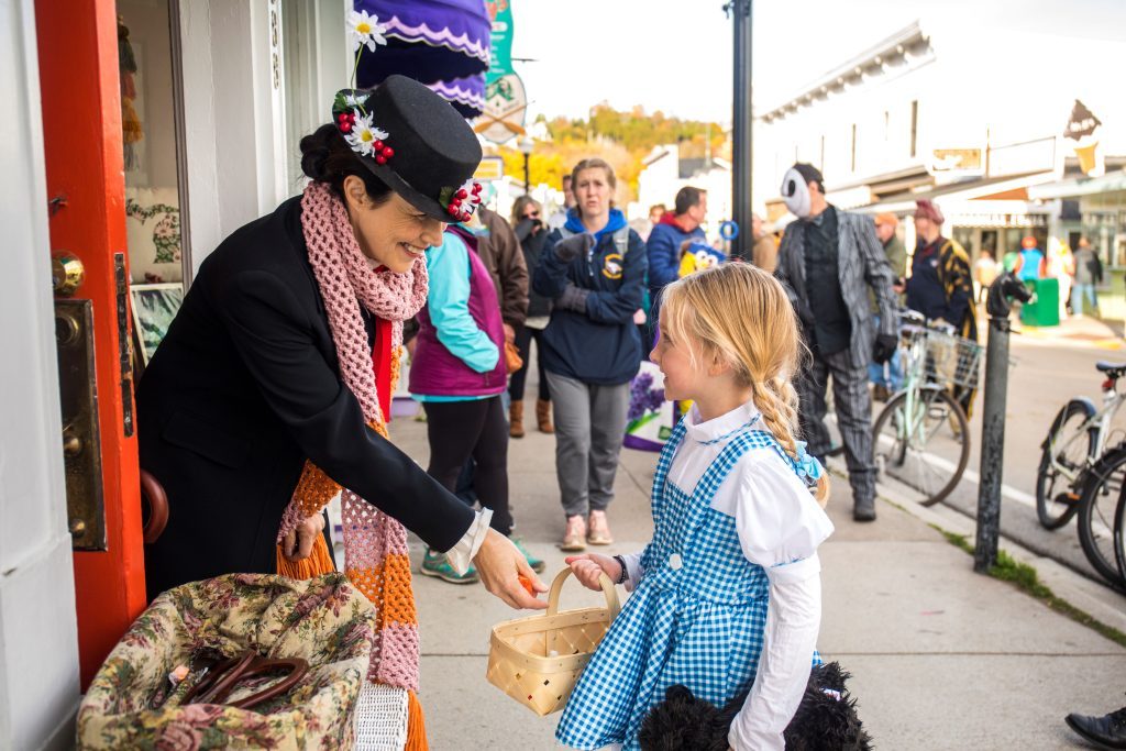 A Mackinac Island shopkeeper puts candy into the basket of a trick-or-treater dressed as Little Red Riding Hood