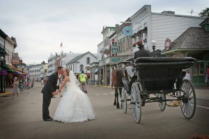 A bride and groom kiss in the middle of Mackinac Island's Main Street as their horse-drawn carriage driver waits nearby