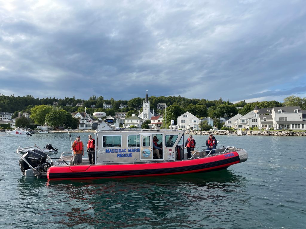 Mackinac Marine Rescue crew stand on the boat in the water off Mackinac Island with Ste. Anne’s Church in the background