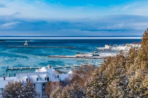 A view of the icy Mackinac Island harbor in winter with snow draped on trees and buildings in the foreground