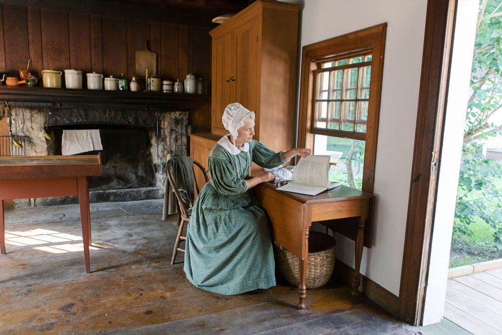 A historical interpreter wearing period clothing from the 1800s reads papers at a desk inside the Biddle House on Mackinac Island