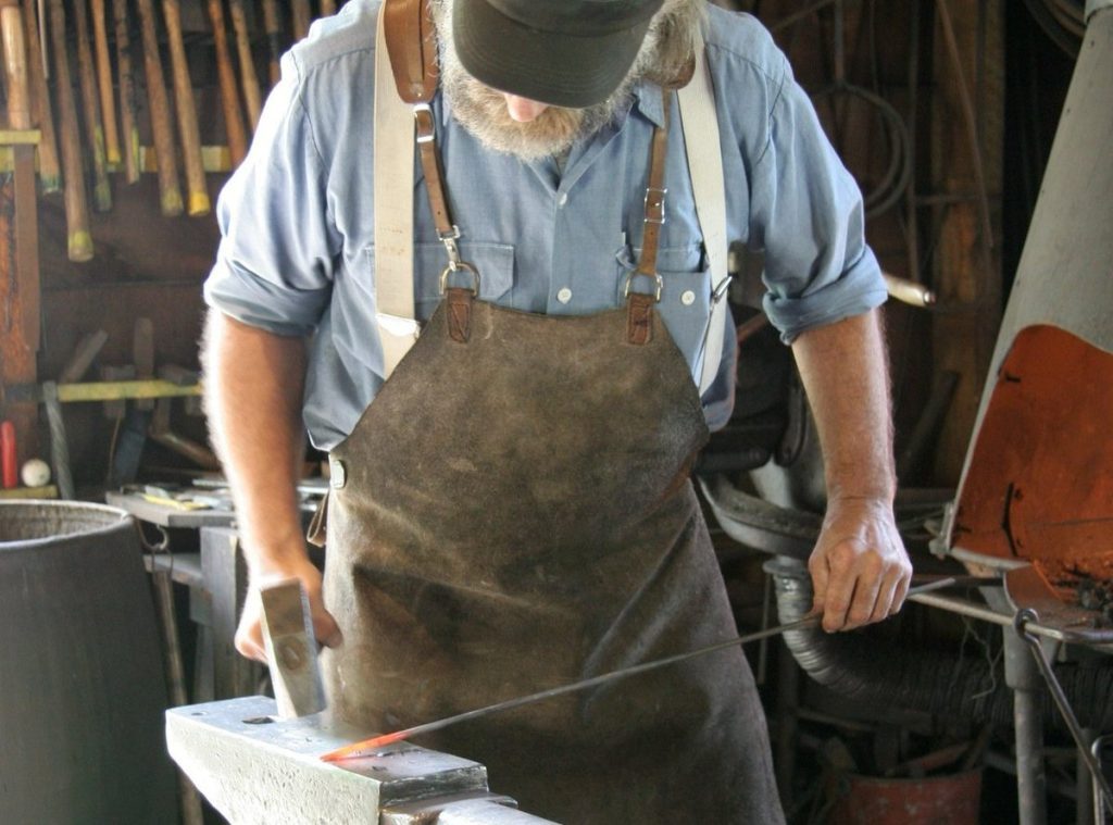 A historical interpreter beats a piece of iron with a hammer inside the Benjamin Blacksmith Shop on Mackinac Island