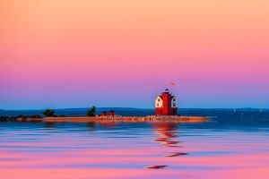 The morning sunrise lights up Round Island Lighthouse, which reflects on the water across from Mackinac Island