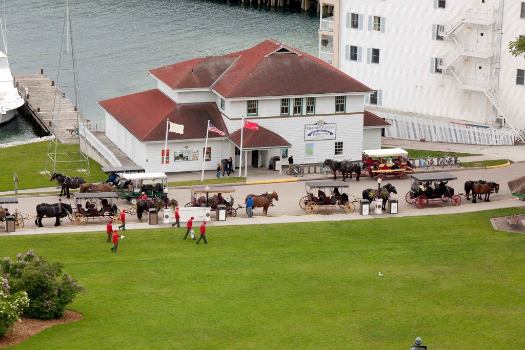 Aerial view of Mackinac Island Visitors Center on the water across from Marquette Park with horse carriages out front