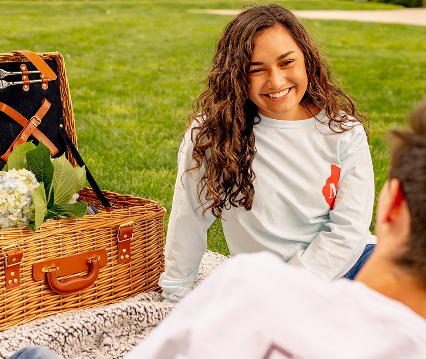 A young woman wearing a Threads of Mackinac t-shirt smiles at a young man while having a picnic on Mackinac Island