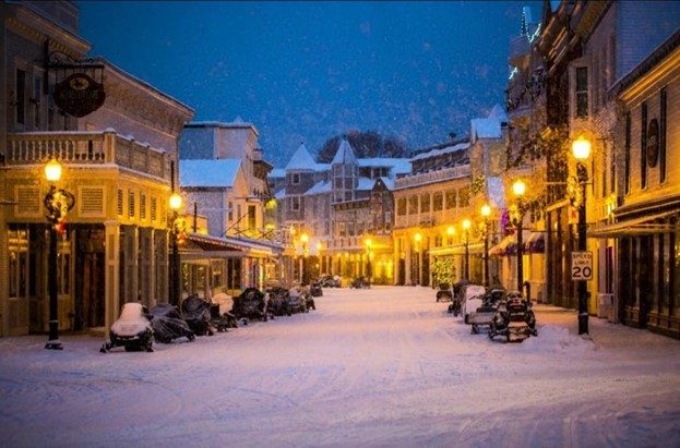 Snowy winter scene of downtown Mackinac Island at night with streetlights aglow and snowmobiles lining street