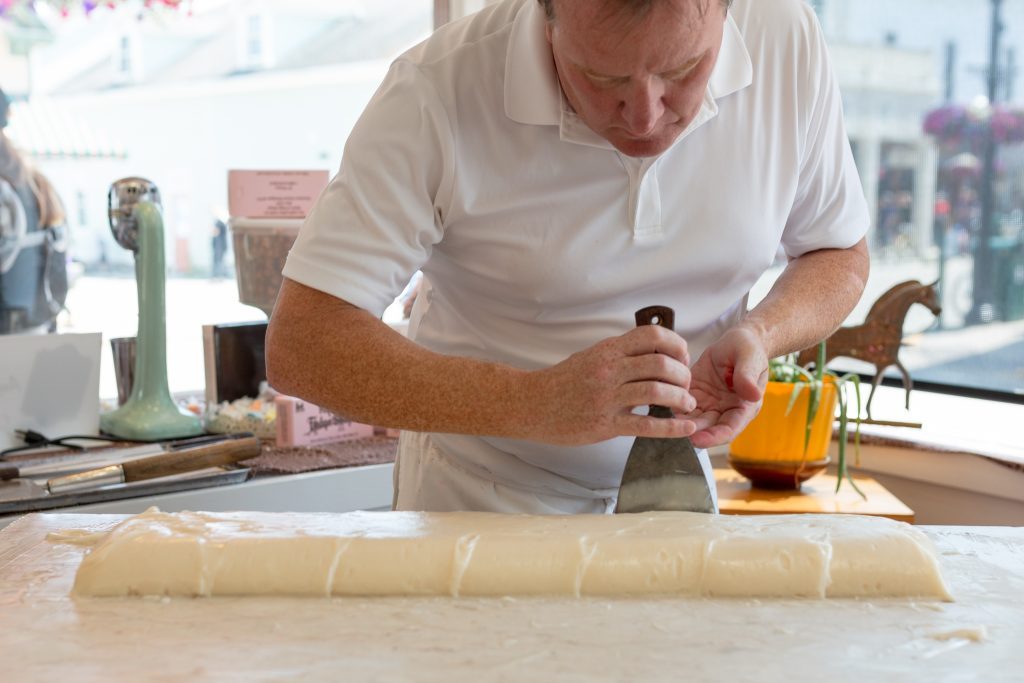 A Mackinac Island fudge maker shapes liquid fudge into a loaf on a marble slab in a downtown storefront