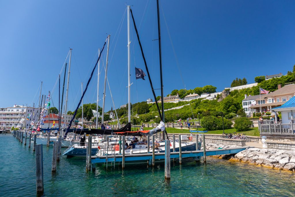 Sailboats line the docks in the Mackinac Island marina on a summer day with Fort Mackinac up on the bluff in the background