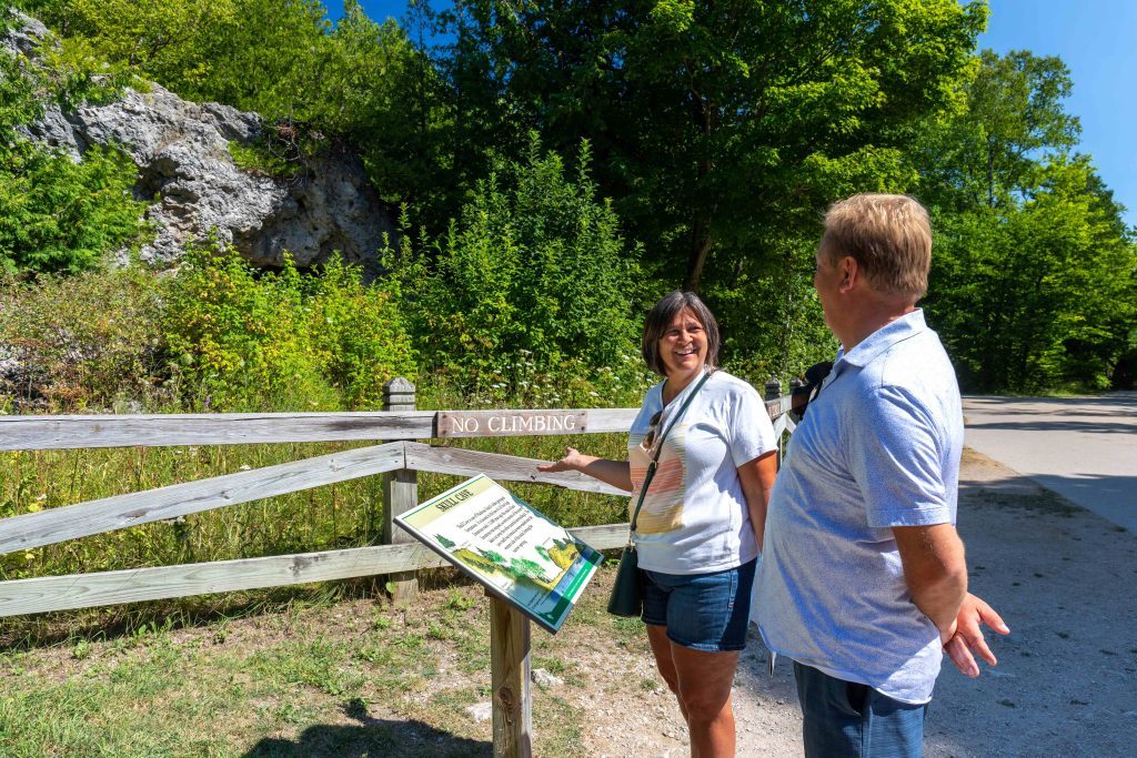 A woman and a man read an interpretive sign near Skull Cave in Mackinac Island State Park