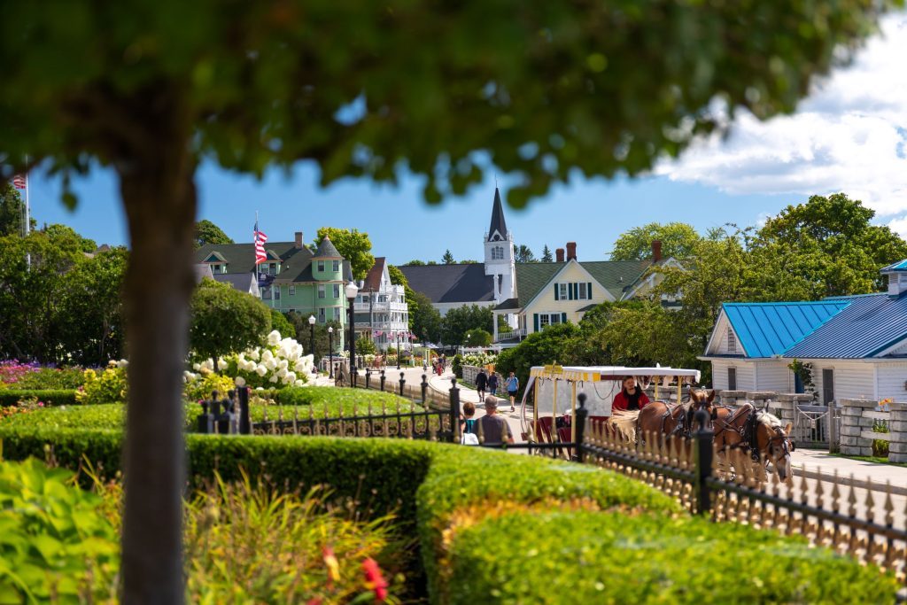 An idyllic Mackinac Island scene featuring a horse-drawn carriage on the street and St. Anne’s Church in the background