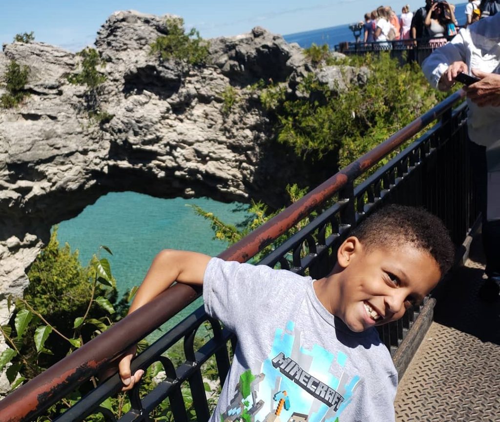 A young boy with a Minecraft t-shirt wraps his arm around the railing at Mackinac Island’s Arch Rock viewing platform