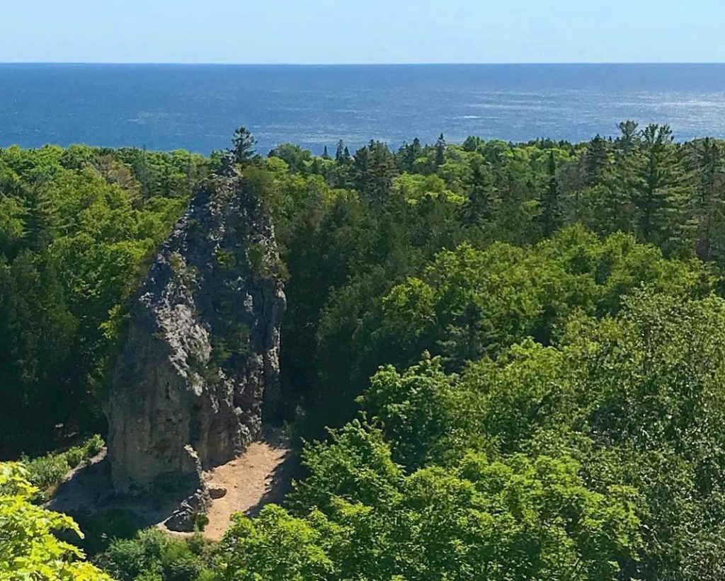 Sugar Loaf rock formation rises out of the Mackinac Island State Park forest with Lake Huron in the background