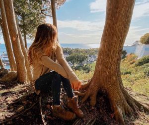 A woman sits in the shade of a tree on a bluff overlooking downtown Mackinac Island