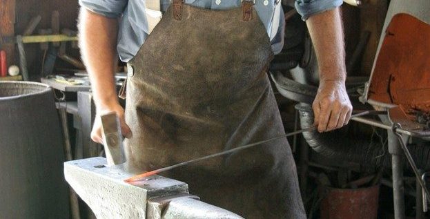 A blacksmith uses a hammer and anvil to pound a hot piece of metal in a shop on Mackinac Island