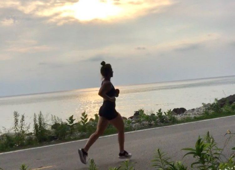 A young woman silhouetted by the rising sun runs along a road by the water on Mackinac Island