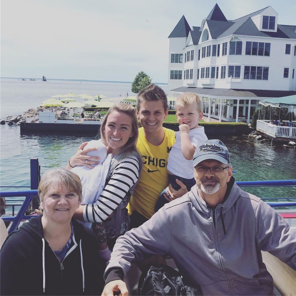 A multigenerational smiles for the camera on the Mackinac Island ferry docks with a hotel and the water in the background