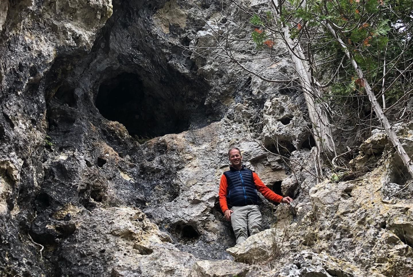 A man stands on a rock face below a cave opening on Mackinac Island