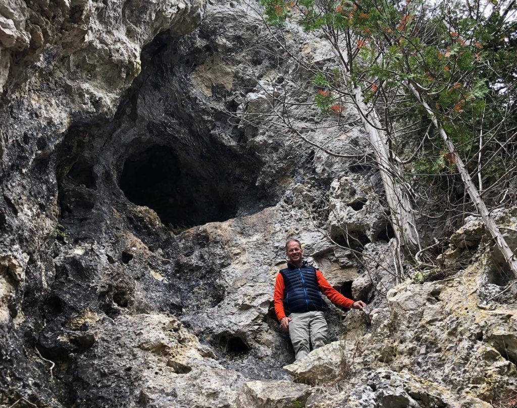 A man stands on rocks below Eagle Point Cave on Mackinac Island