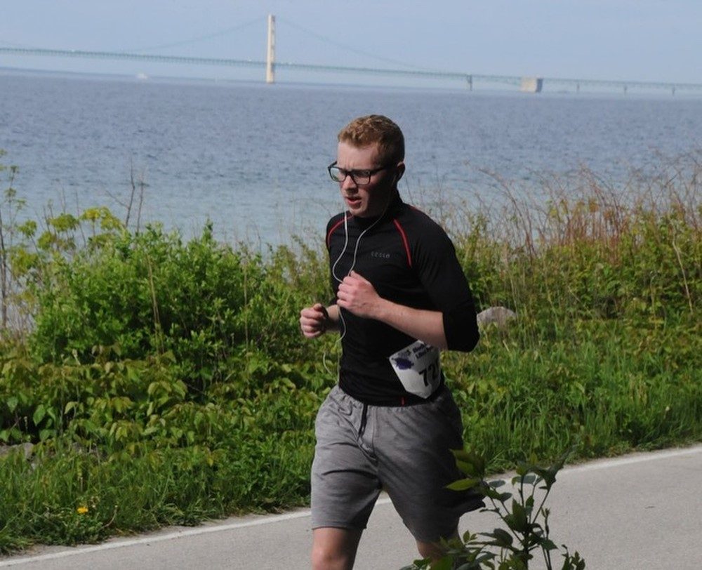 A young man runs along the lakeshore on Mackinac Island with the Mackinac Bridge in the background