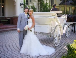 A happy bride and groom stand outside Mackinac Island's Inn at Stonecliffe next to a horse-drawn carriage