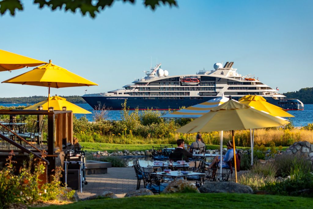 A cruise ship passes by Mackinac Island as people dine at a waterfront restaurant