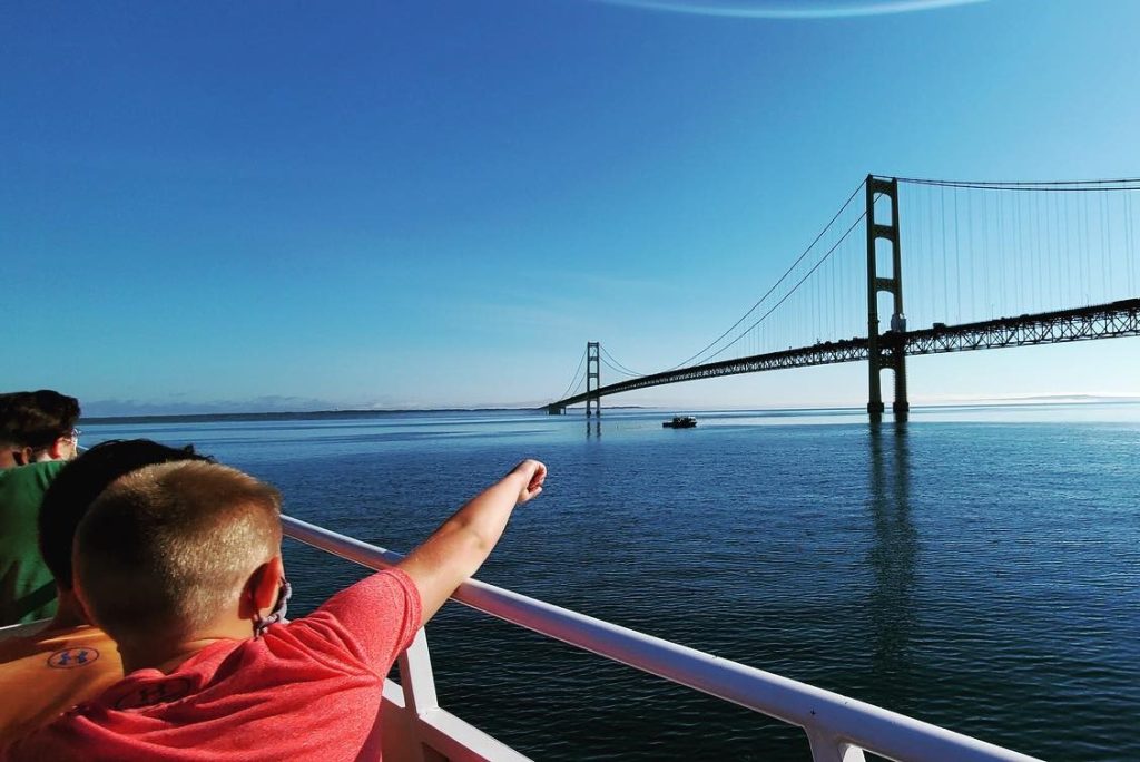A boy points toward the Mackinac Bridge while riding a Mackinac Island ferry boat on a sunny day